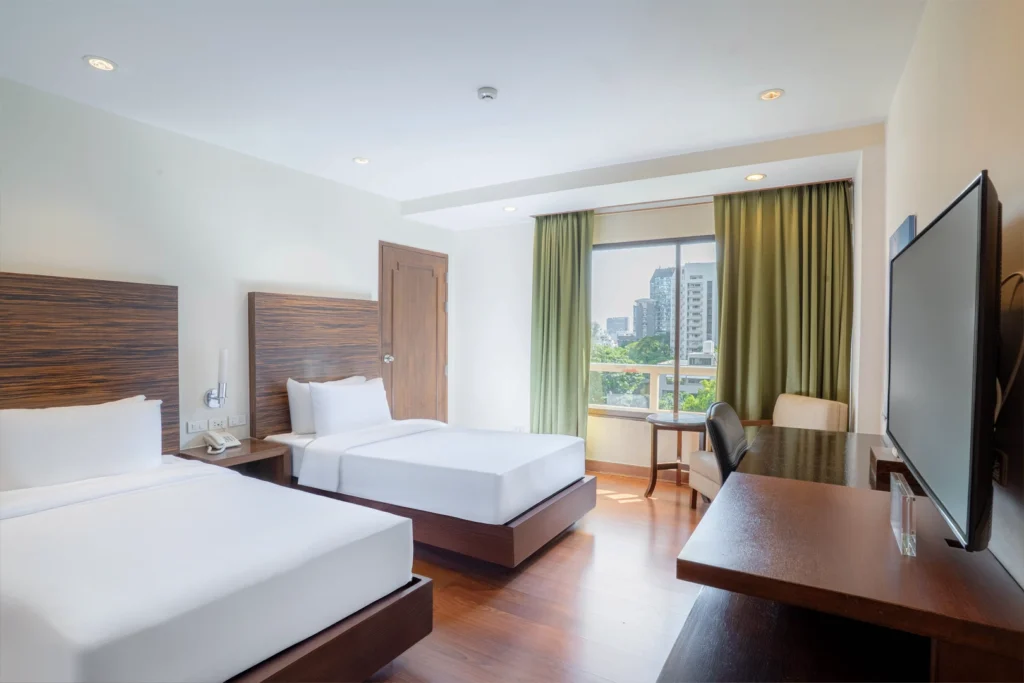 Deluxe Twin Room at a hotel near BTS Phrom Phong, with two single beds, city view window, work desk, and wooden interior.