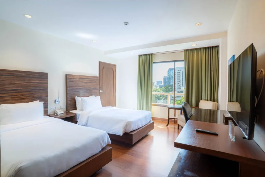 Deluxe Twin Room at a hotel near BTS Phrom Phong, with two single beds, city view window, work desk, and wooden interior.
